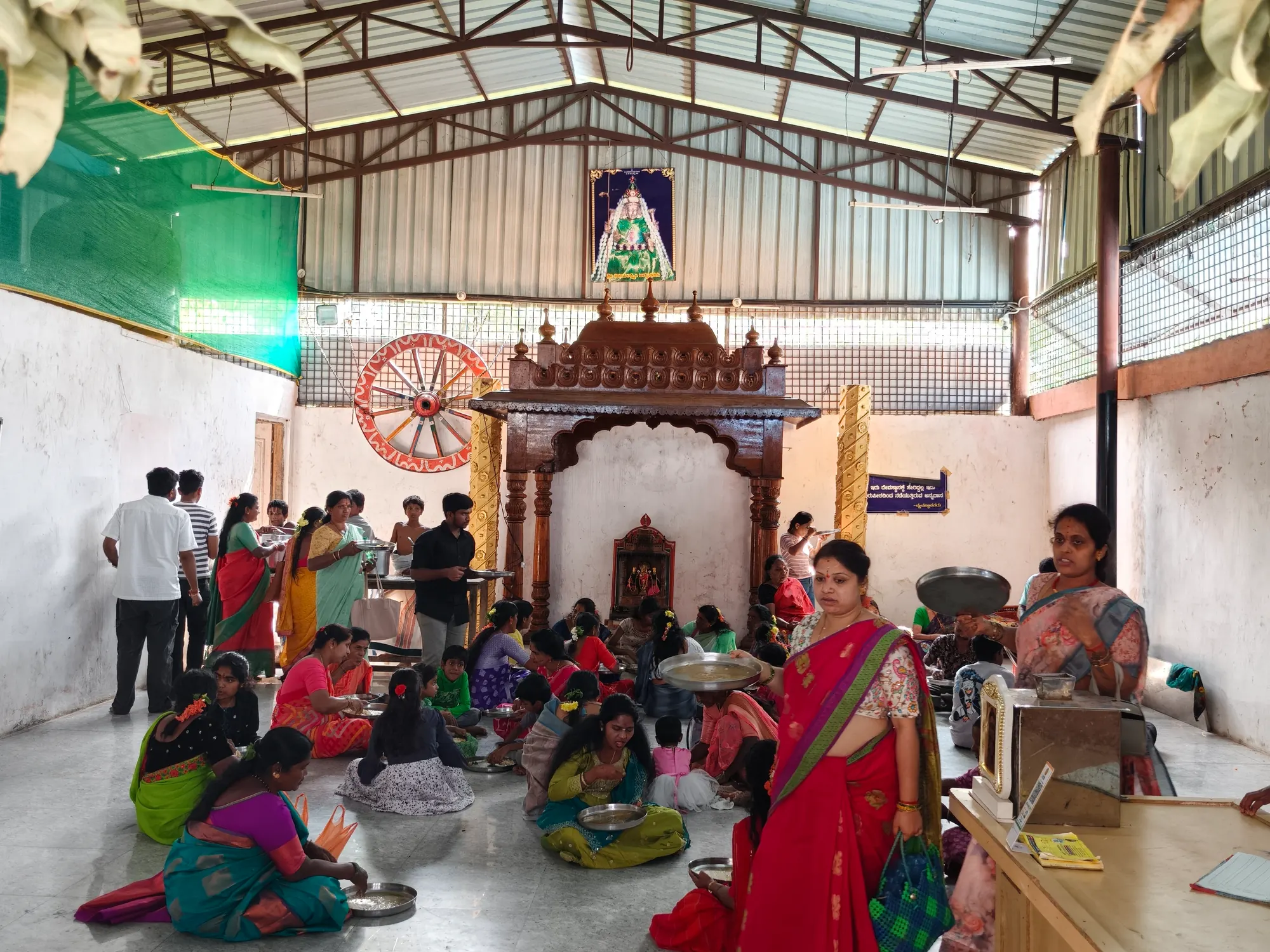 The annadana hall full on a festival day, women and children seated in rows across the floor eating while the serving vessels are carried between them
