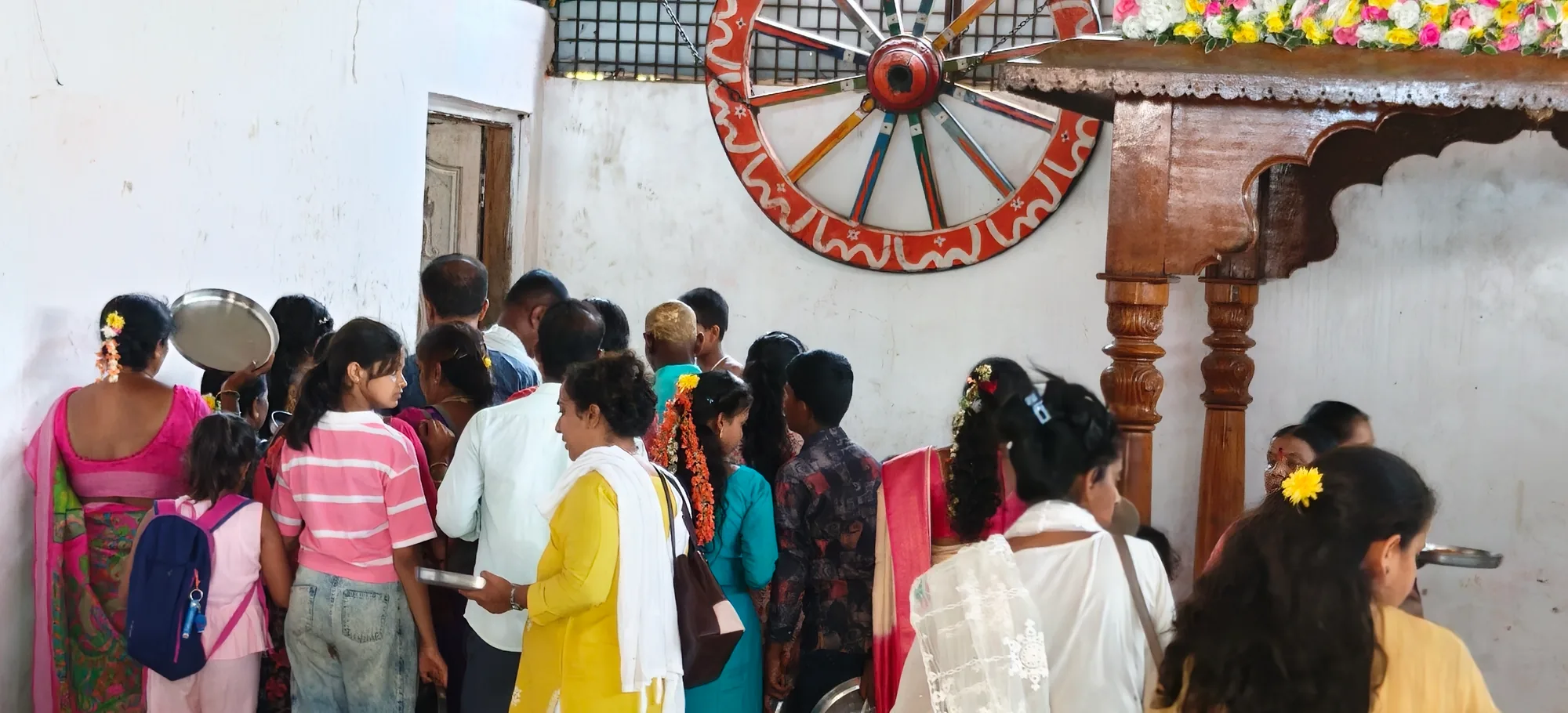 The line for the meal winding past a painted wooden cartwheel mounted on the hall wall, families with plates in hand waiting their turn under the flower-hung canopy