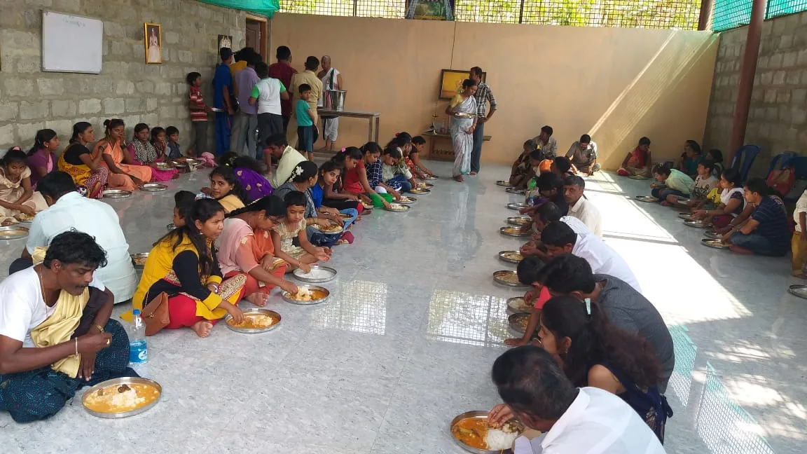 The annadana hall at the meal — families and children seated in long rows down both sides of the floor with steel plates of rice in front of them, the servers working the aisle between