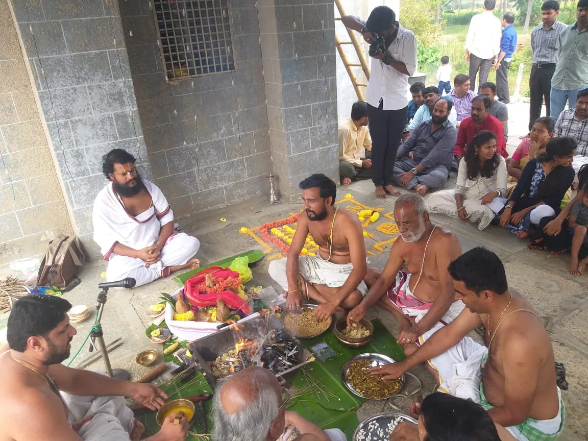 Vaidikas seated around a homa on a bare concrete floor under a portico, the people who came for it seated in a ring behind
