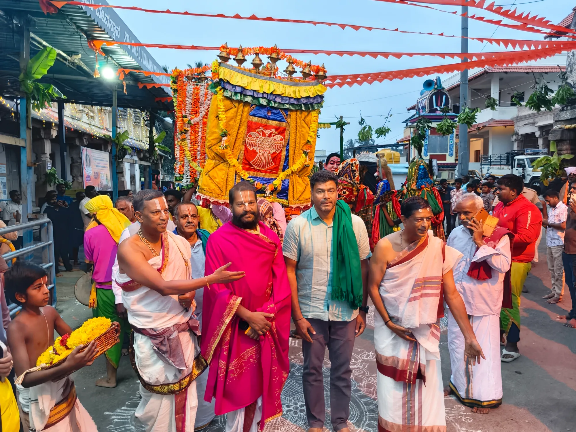 The palanquin carried through the town at first light under strings of orange bunting, the vaidikas walking ahead of it