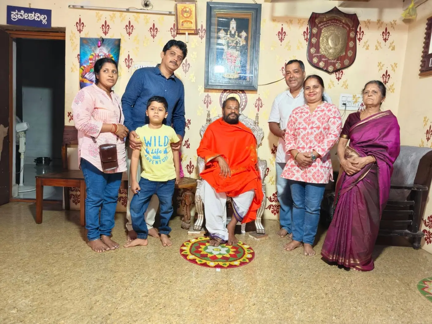 A family standing on either side of Guruji seated in an orange shawl, their small boy held between them, a rangoli drawn on the floor at his feet