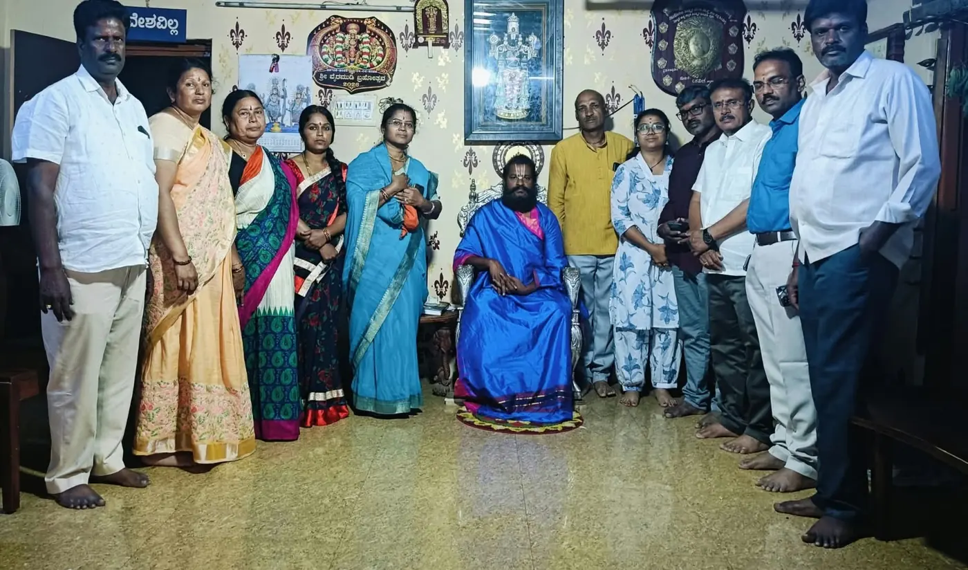A large family — a dozen of them, in sarees and shirtsleeves — standing in a line across the room on either side of Guruji seated in a blue shawl