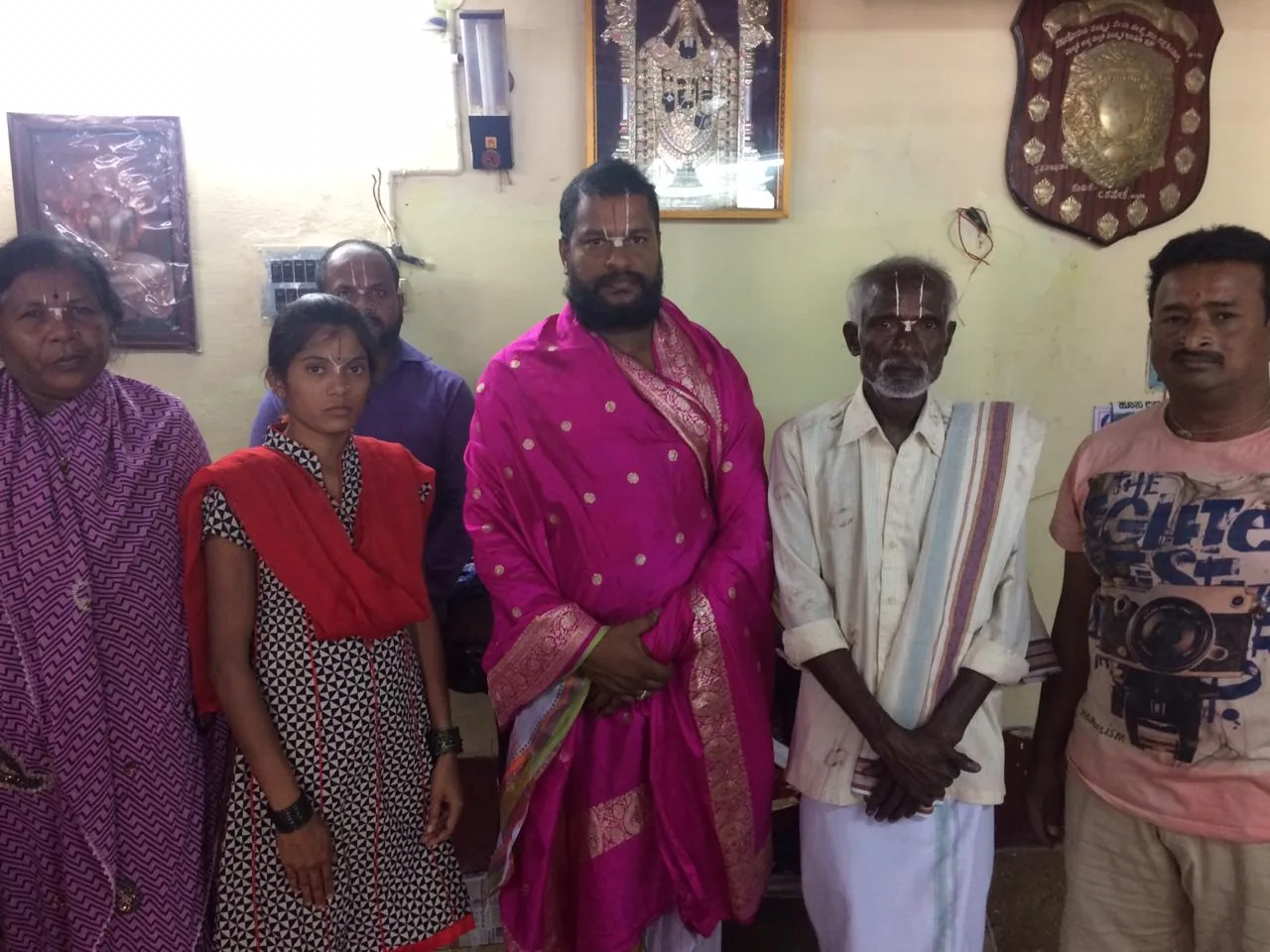 Guruji in a rose-pink shawl standing among a village family who have come to see him — an elderly man, two women and a girl — in the reception room of the mandira