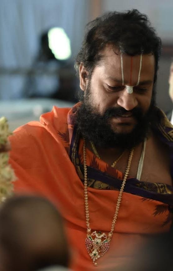 Guruji in saffron robes with head bowed in prayer during a temple ceremony