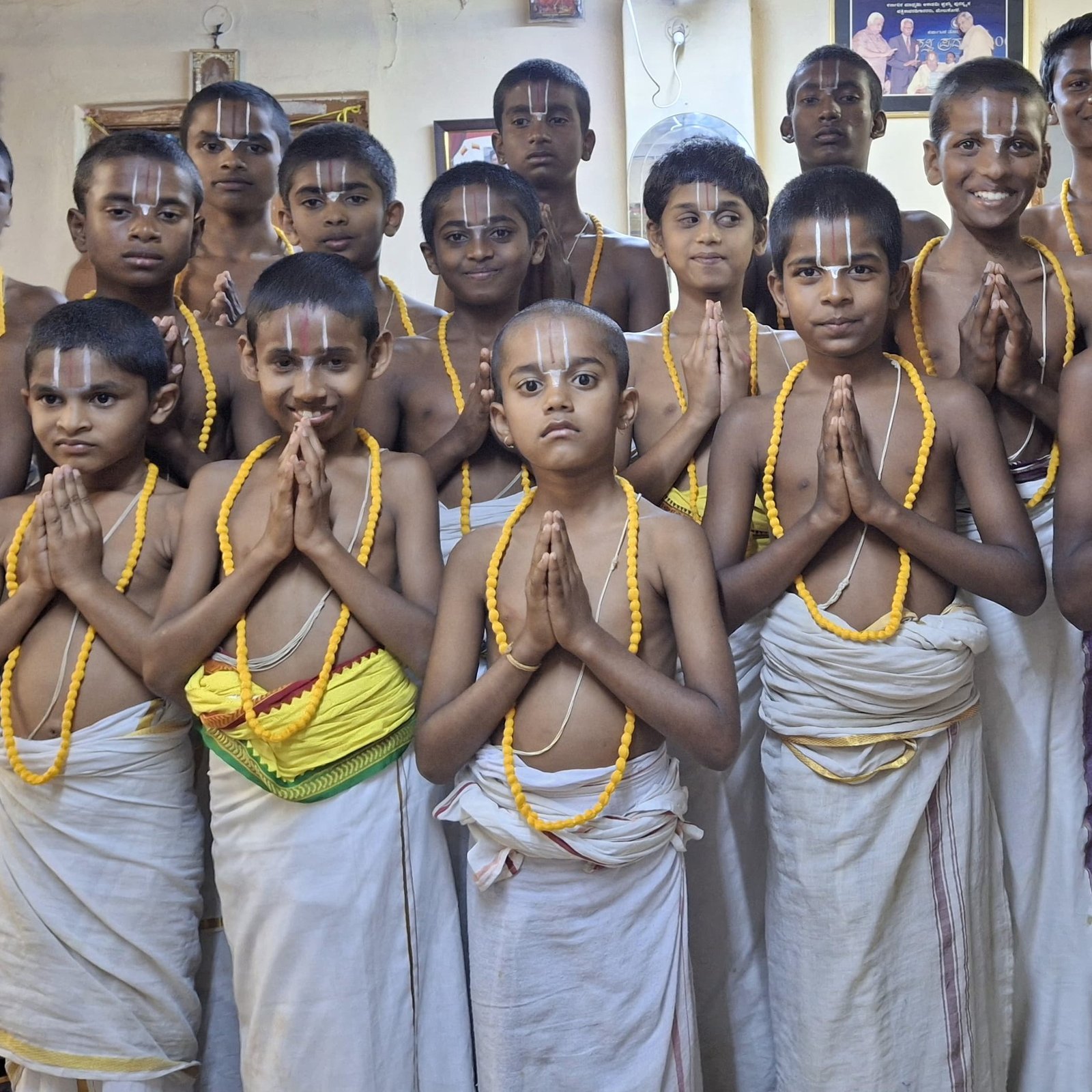 A group of gurukulam students wearing yellow flower garlands, standing together with palms joined in namaskara