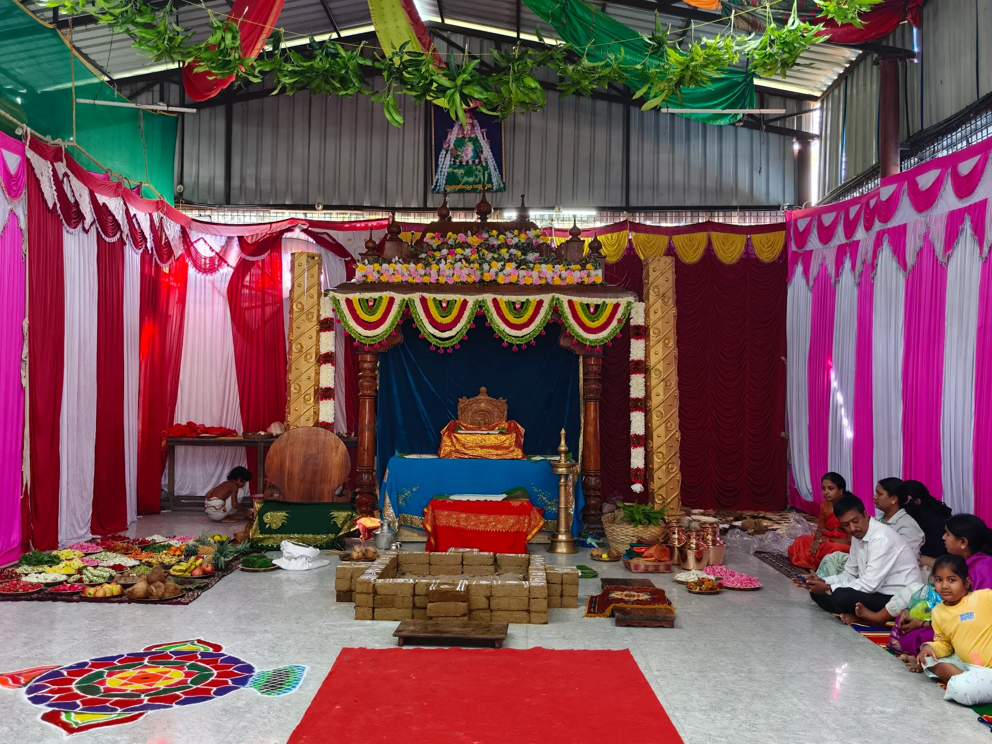 The whole hall laid out for a function: the decorated mandapa at the far end, the brick homa kunda built in the middle of the floor, and a rangoli drawn at the near edge
