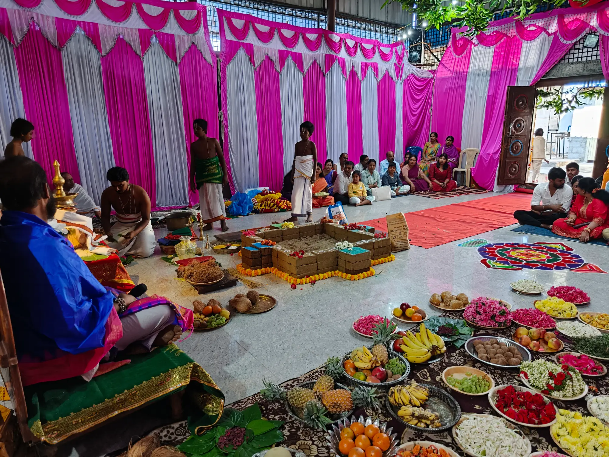 The brick homa kunda raised in the middle of the pandal and ringed with marigold, priests seated at one side of it and the offerings spread out at the other