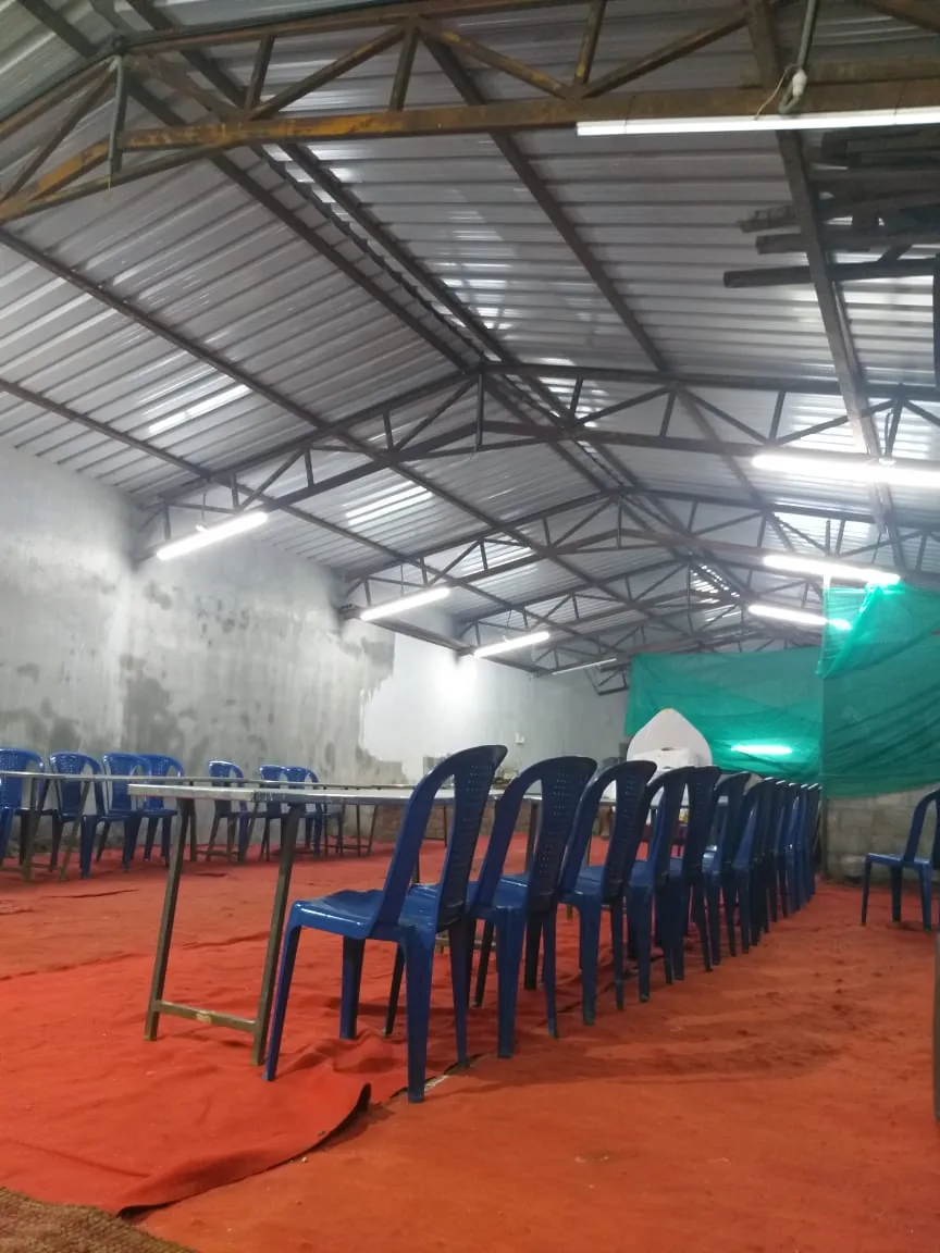 Rows of blue chairs and long steel serving tables set out down the length of the empty hall on a red floor covering