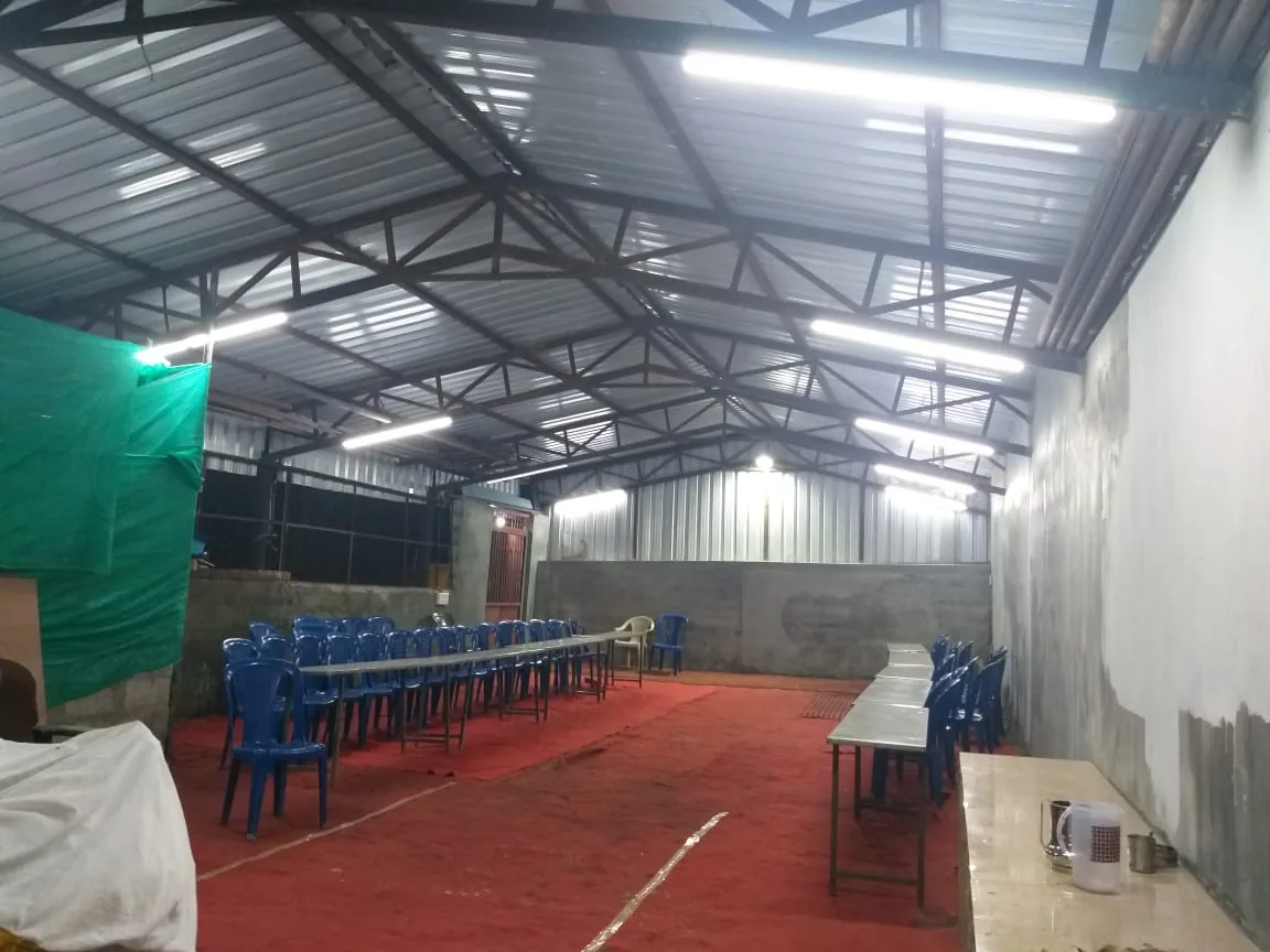 The function hall under its steel roof with the chairs stacked in rows and the serving tables laid along one wall, before a function