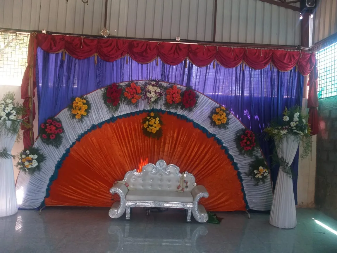A fan-shaped backdrop of orange, purple and silver drapes hung with flowers, a silver settee set on the stage in front of it