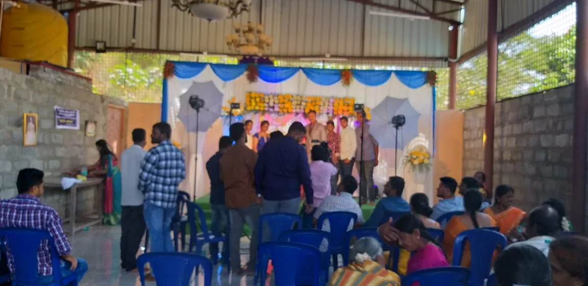 A reception in progress in the hall — the party standing on the decorated stage while the guests sit in rows of chairs below