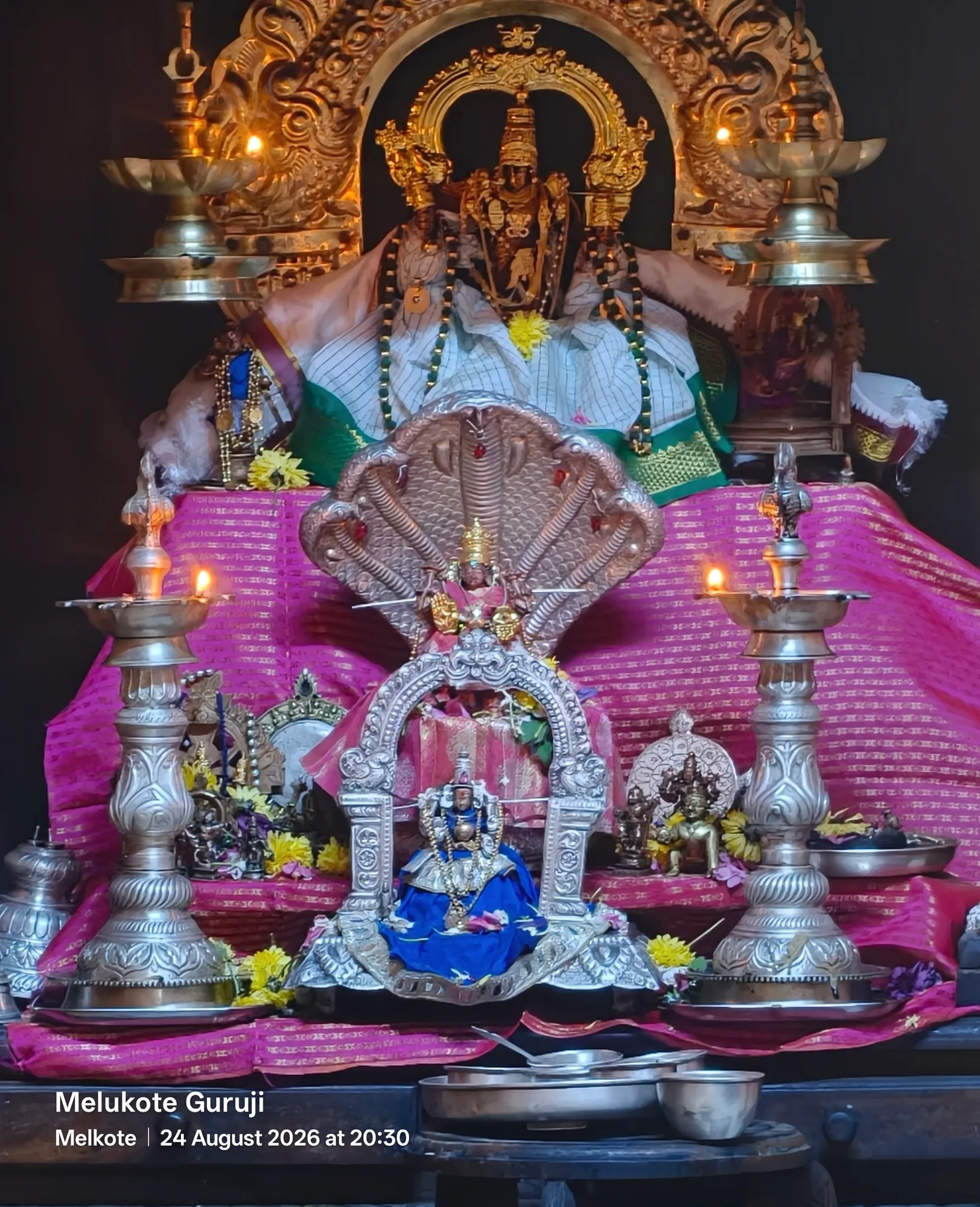 The whole altar of the mandira dressed for a festival — the deities in white and green above, a silver naga hood and a small shrine below, lamps and vessels ranged across the front