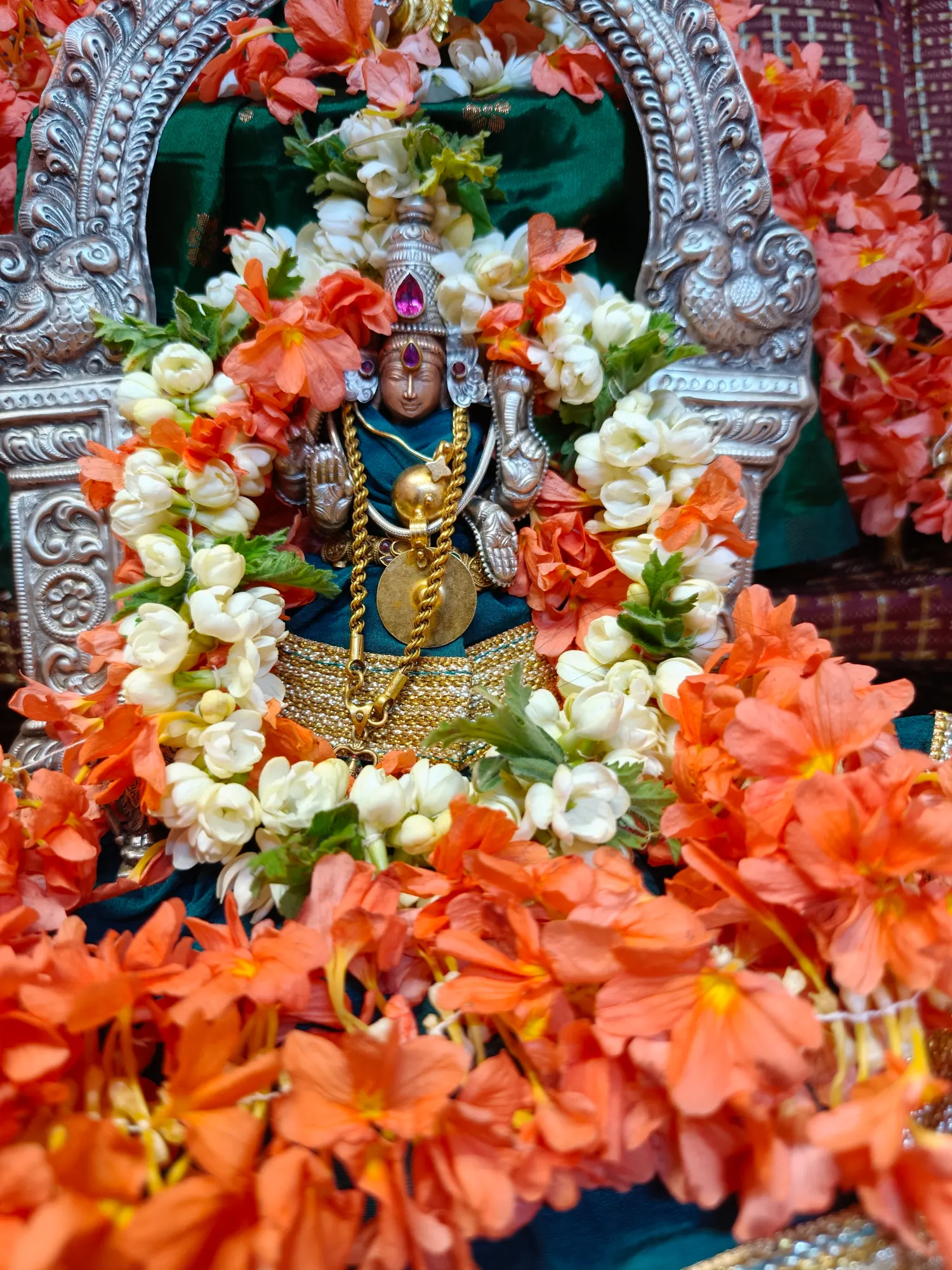 A garlanded murti in a silver frame, deep in jasmine and orange blossom heaped up on every side of it