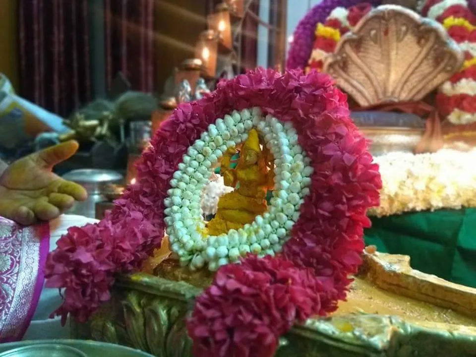 A thick garland of magenta and pale green flowers laid across the seat of the mandira shrine, a small gilded murti at its centre