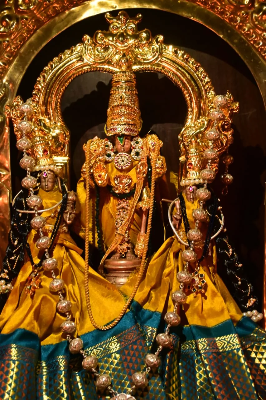 The utsava murti under a heavy gold crown, hung with strings of pearls and dressed in yellow and green silk