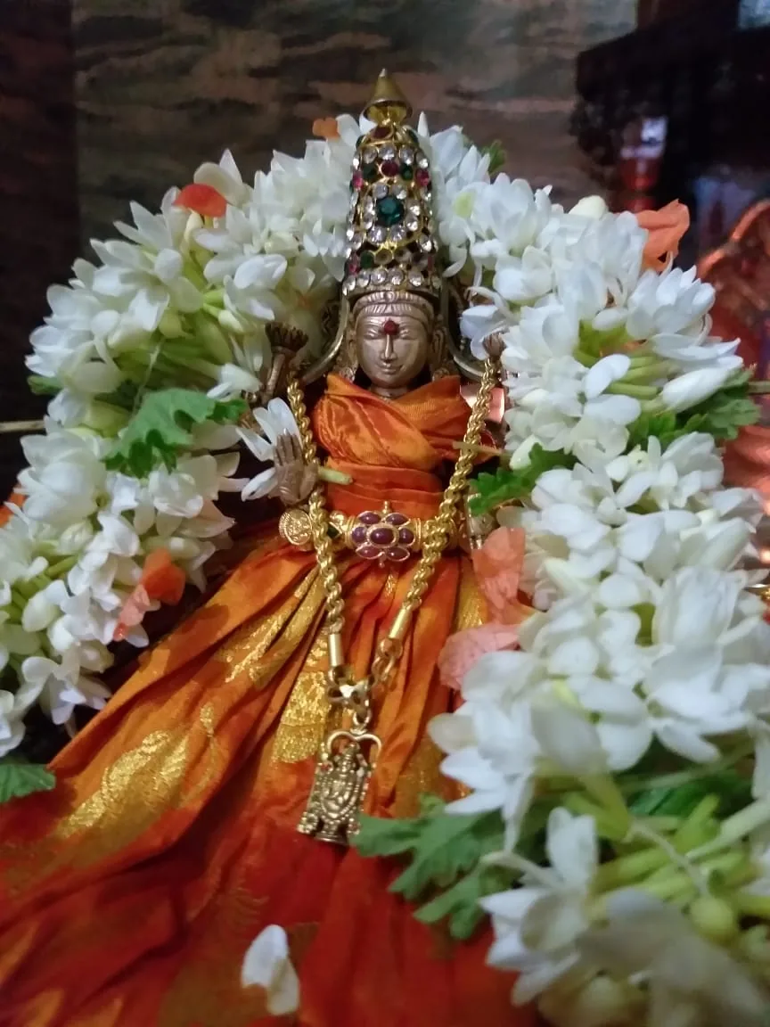 A small crowned bronze murti in orange silk, banked all round with jasmine and marigold in the pooja mandira