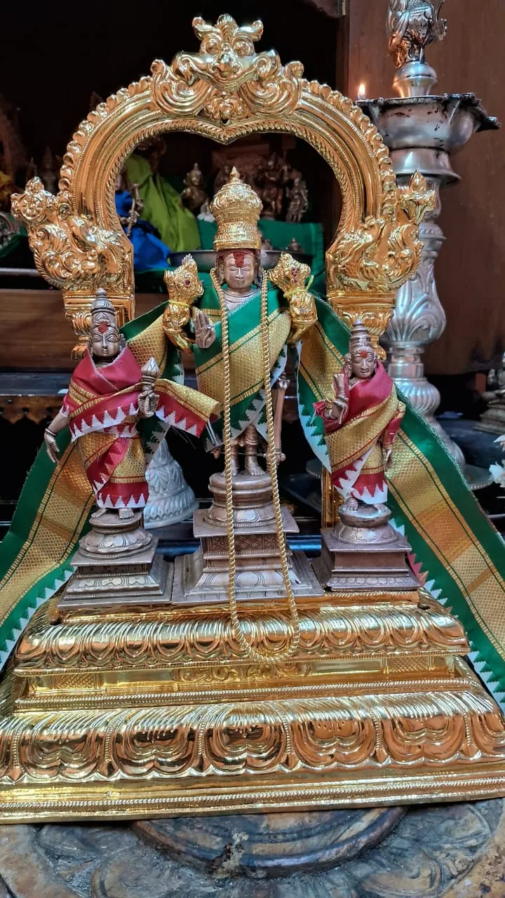 Three murtis standing on a gilded platform beneath a carved golden arch, dressed in green and red bordered silk