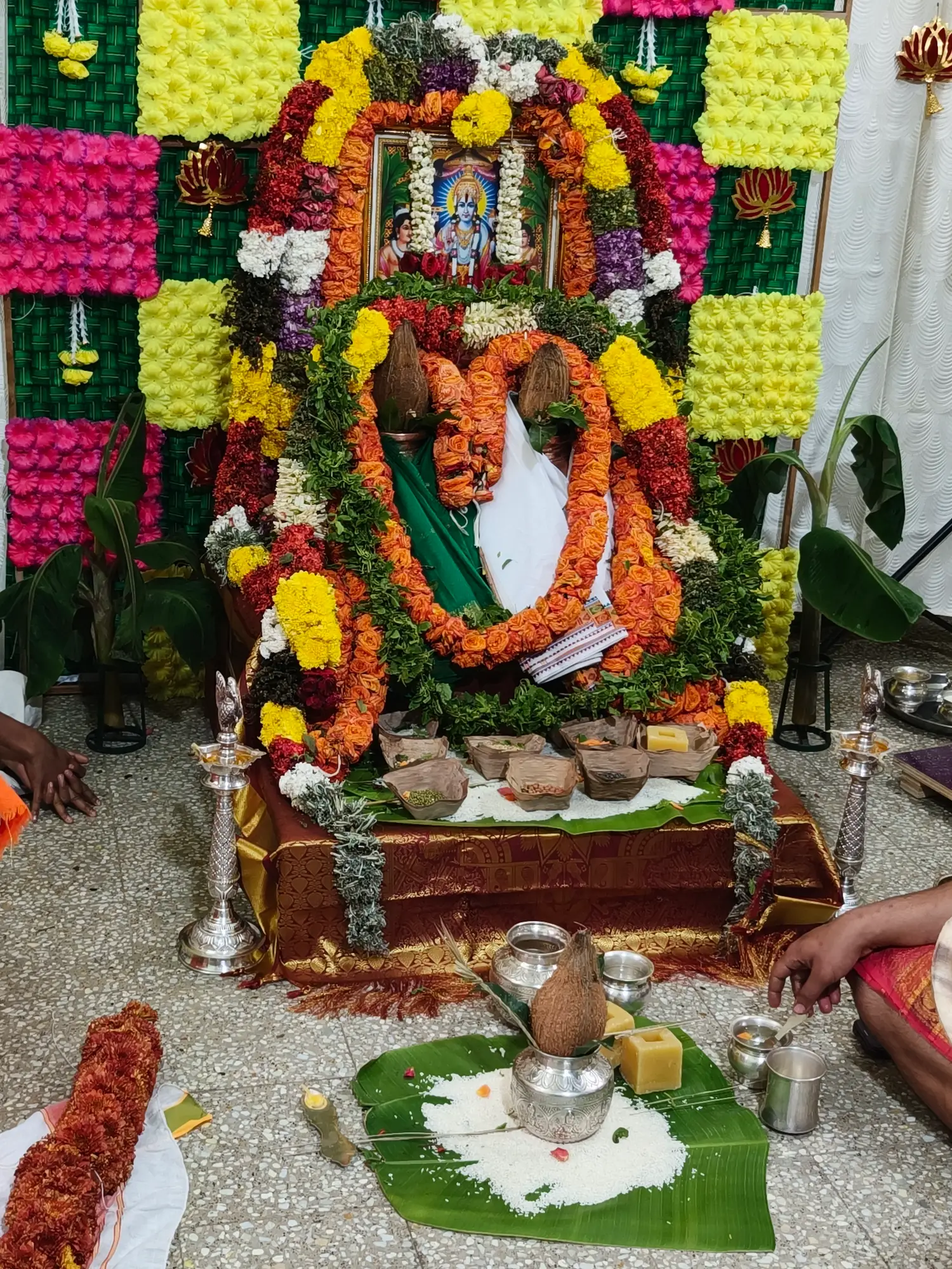 A garlanded image of the Lord beneath a great arch of orange and marigold flowers, with coconut-topped kalashas, banana leaves and heaped rice set out in front of it