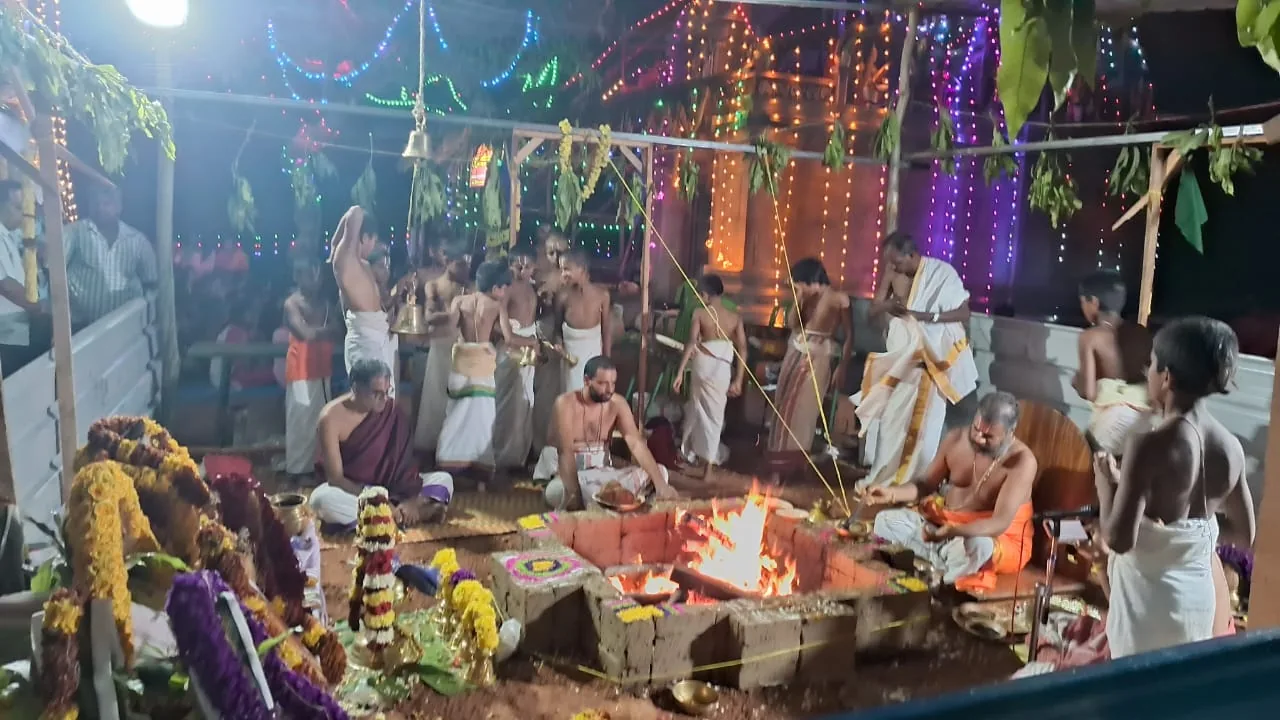 The yaga shala raised beside a temple for its consecration — vaidikas seated in a ring around the brick homa kunda with the fire burning in it, mango leaves strung overhead and coloured lights along the canopy behind