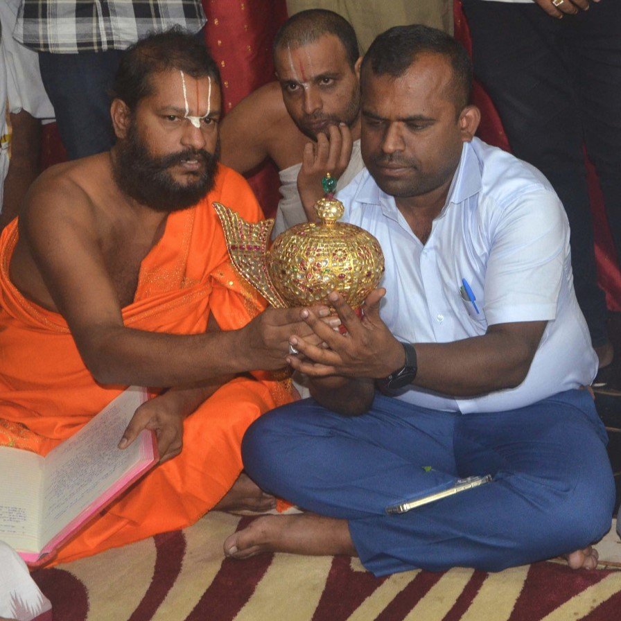 Guruji in saffron robes holding the temple's jewelled golden crown alongside a temple official during the festival arrangements