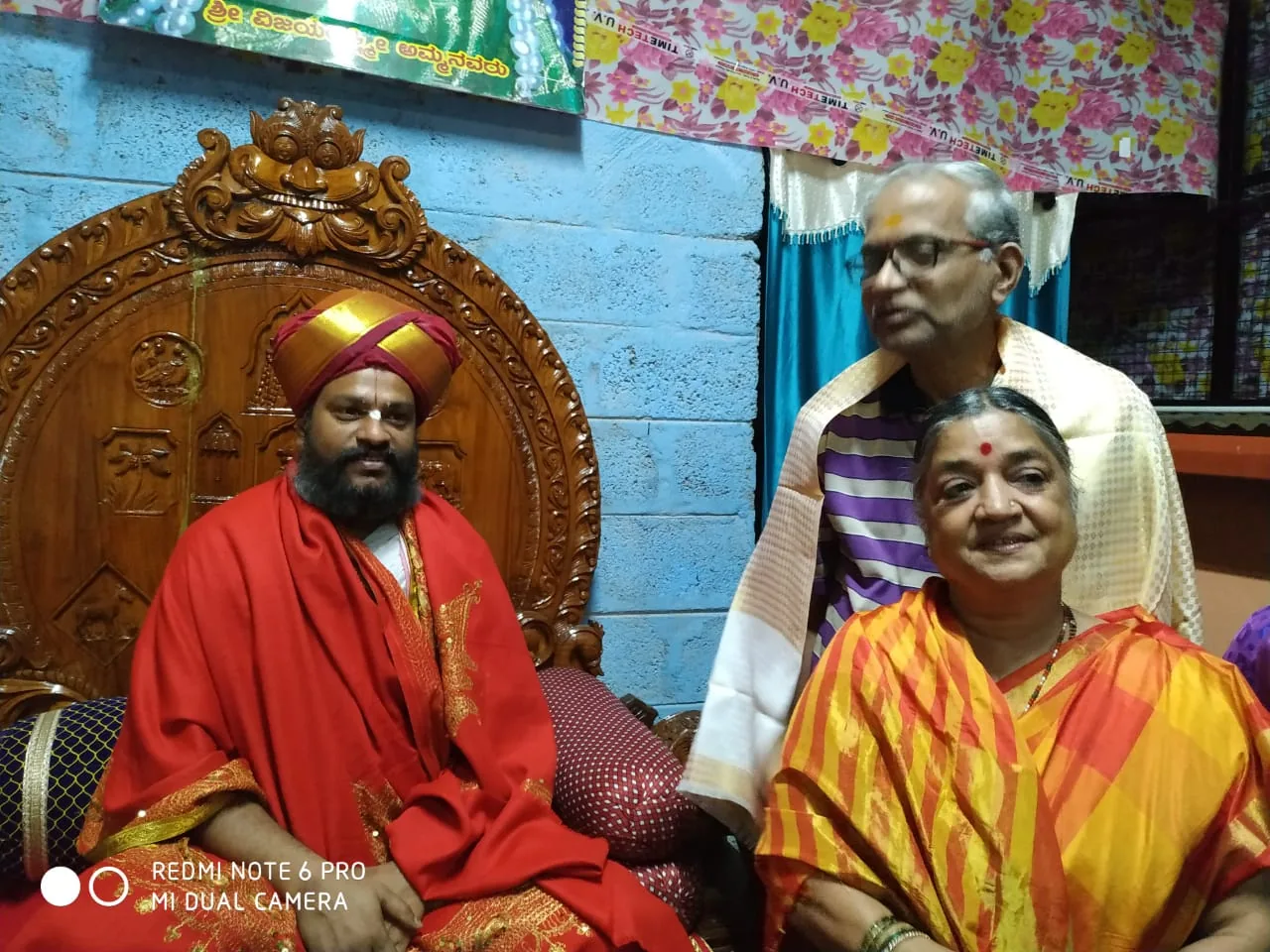 The trustee of the Sringeri Peetha and his wife standing beside Guruji, seated in red on the carved wooden throne of the mandira