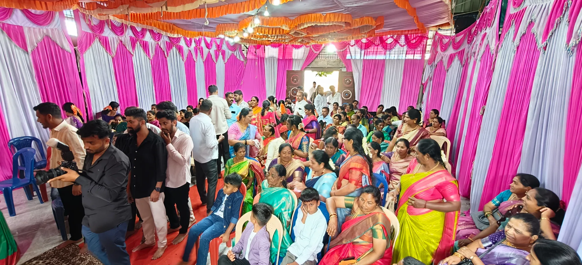Guests filling the hall in rows of chairs under pink and white drapes while the ceremony goes on at the far end