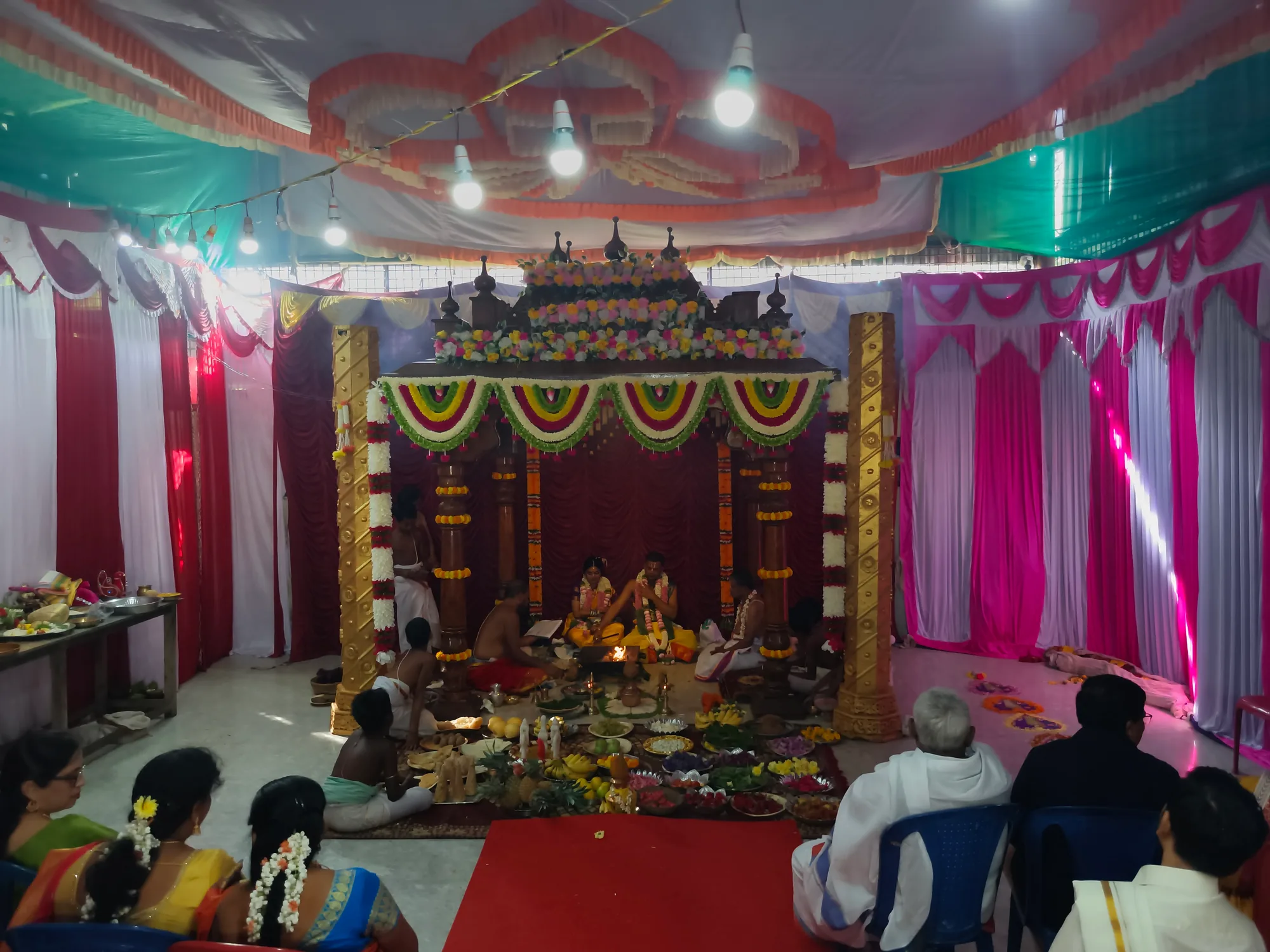 The hall packed with seated guests in silk sarees under pink and white drapes, the mandapa at the far end