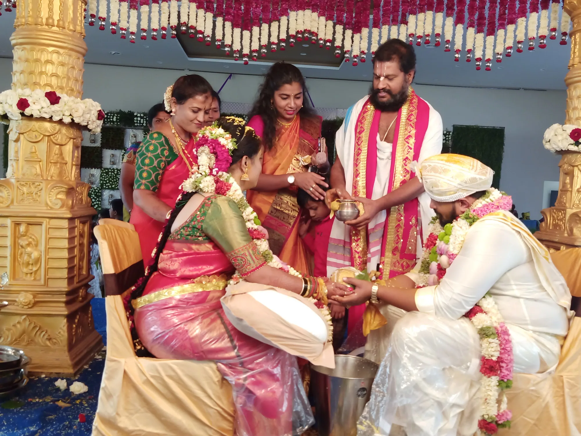 The groom in a gold turban and the bride's family passing a small vessel between them at the rite, the women of the house standing behind