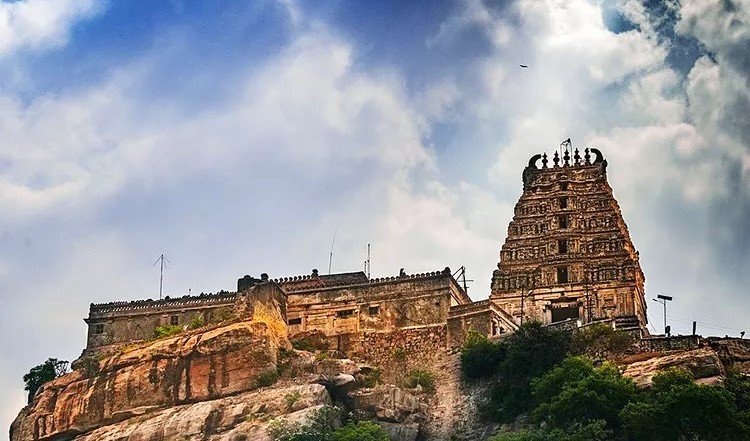 The Yoga Narasimha temple and its gopuram standing on the rocky hilltop above Melukote against a clouded sky